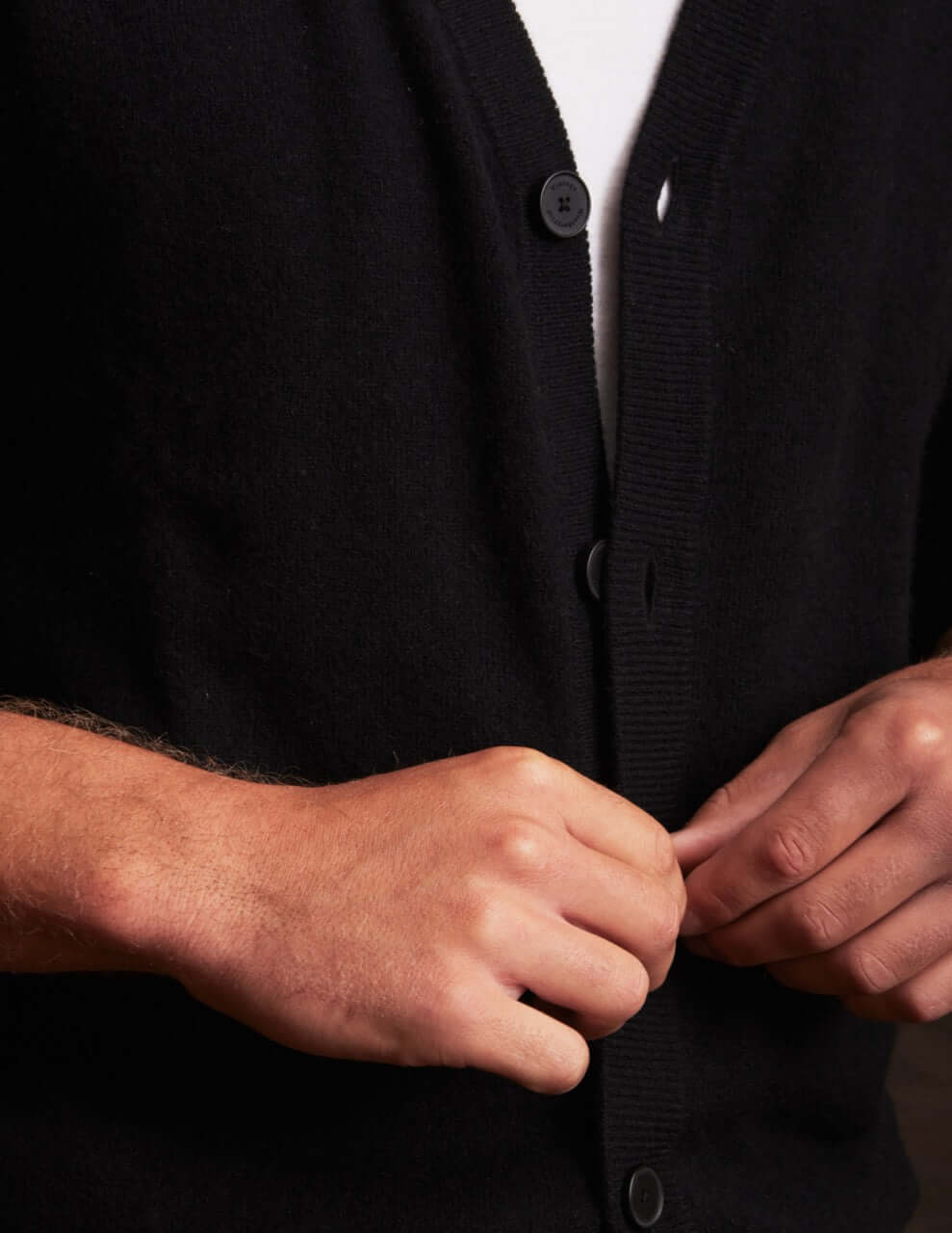 Model adjusting buttons on a soft black cashmere cardigan, showcasing elegant craftsmanship and comfortable fit.