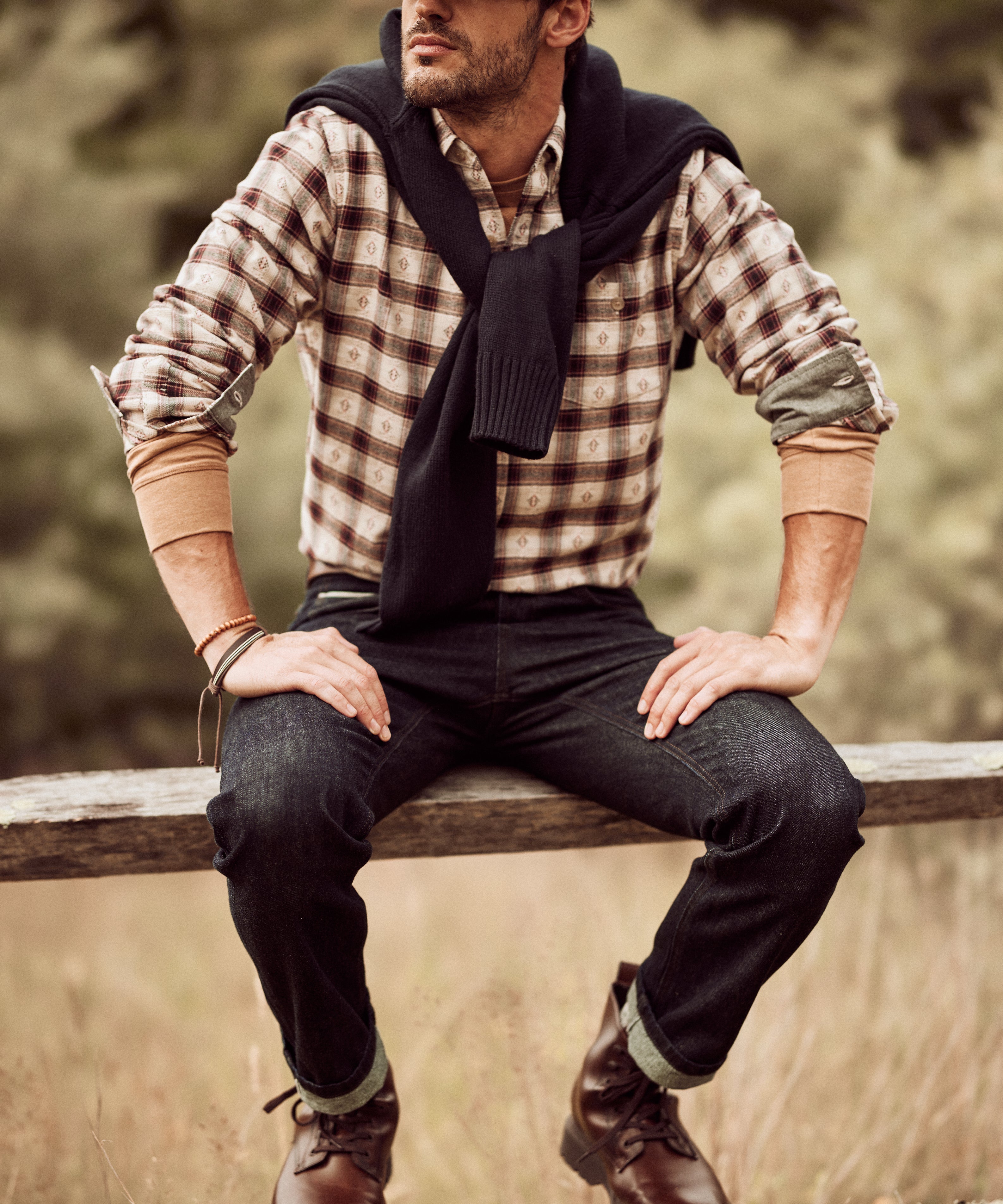 Man wearing Long Sleeve Brushed Flannel in Merlot, sitting on a fence, styled with jeans and a cap.