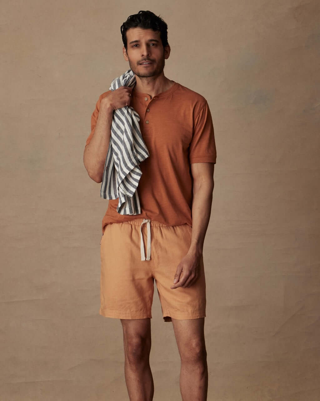 Model wearing 7" linen shorts in biscuit with a casual shirt and beach towel, perfect for warm weather outings.