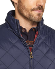 Close-up of a man wearing a navy diamond quilted vest with a zip closure and stand-up collar.
