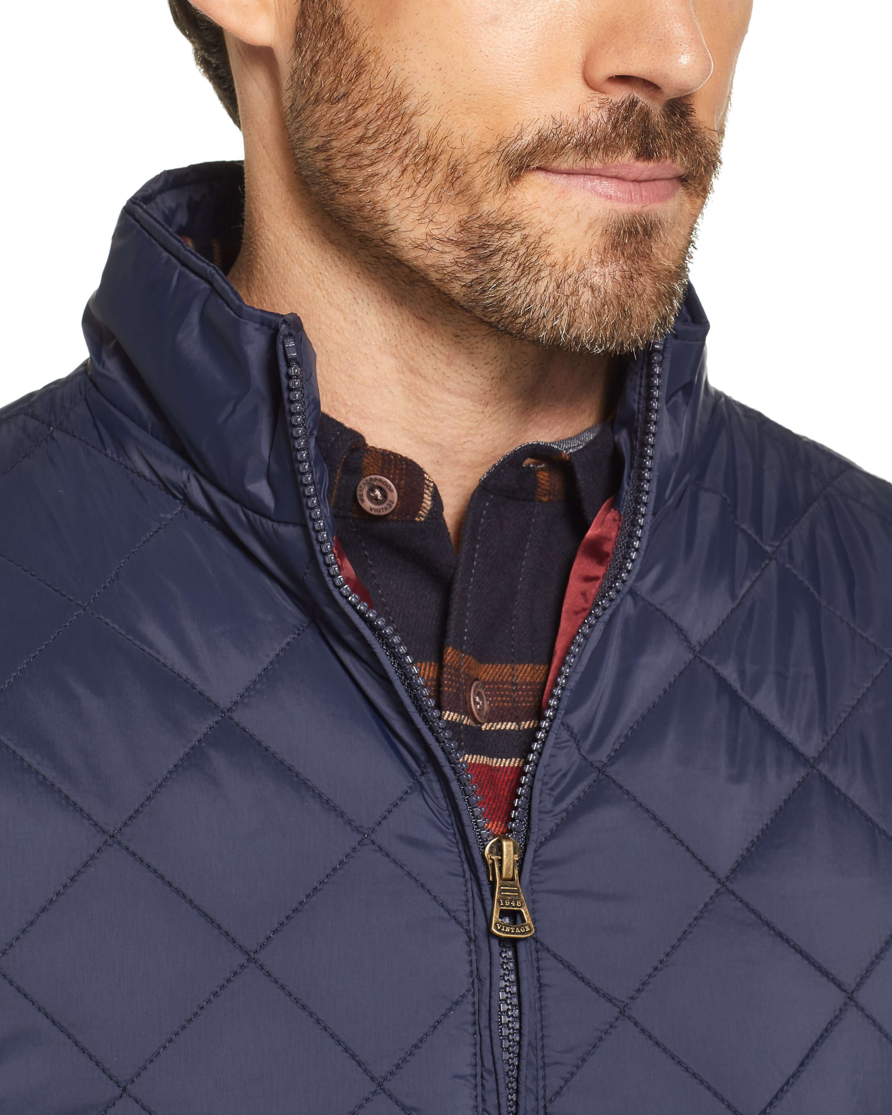 Close-up of a man wearing a navy diamond quilted vest with a zip closure and stand-up collar.