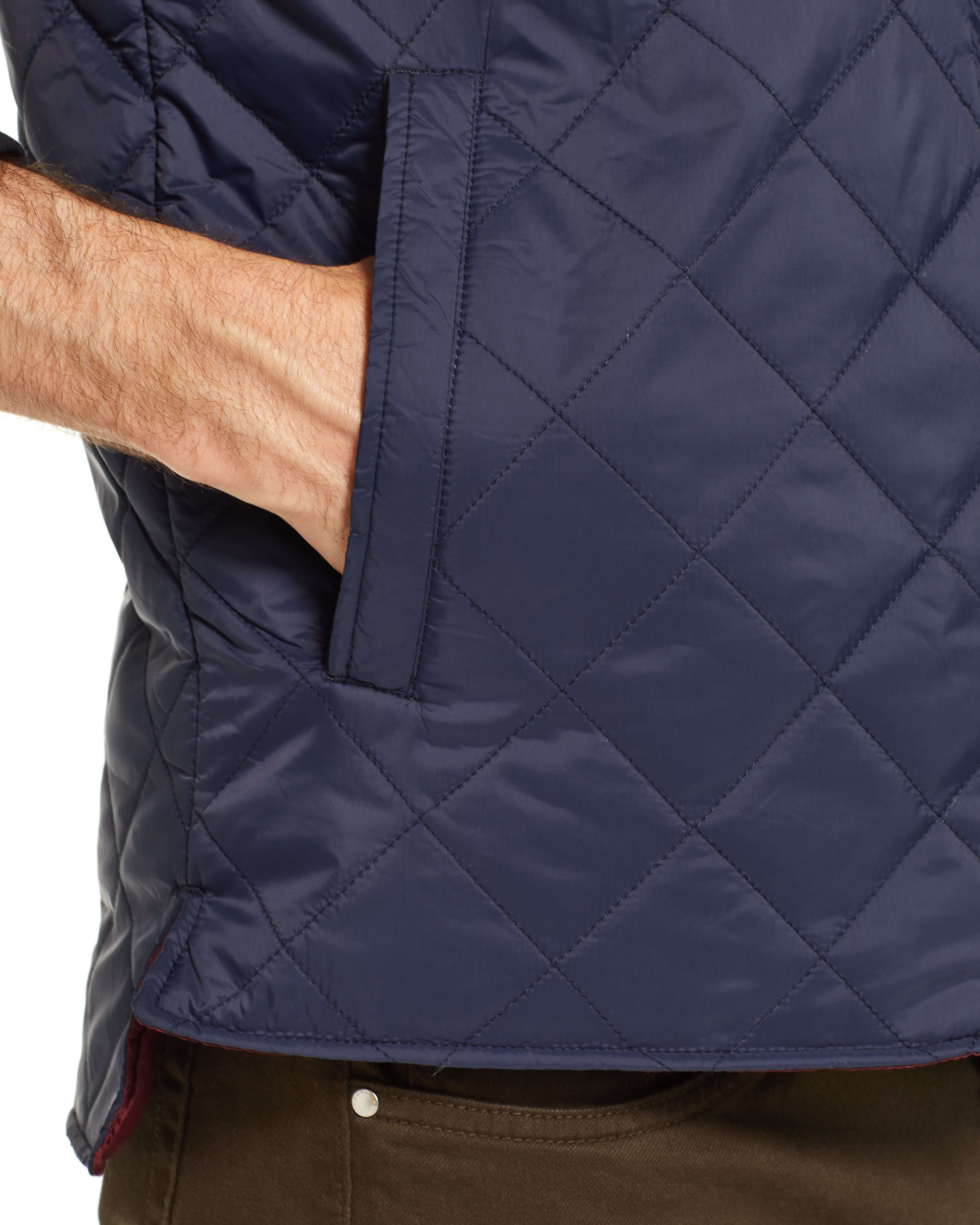 Close-up of a hand inside the pocket of a navy diamond quilted vest, showcasing its lightweight, windproof design.