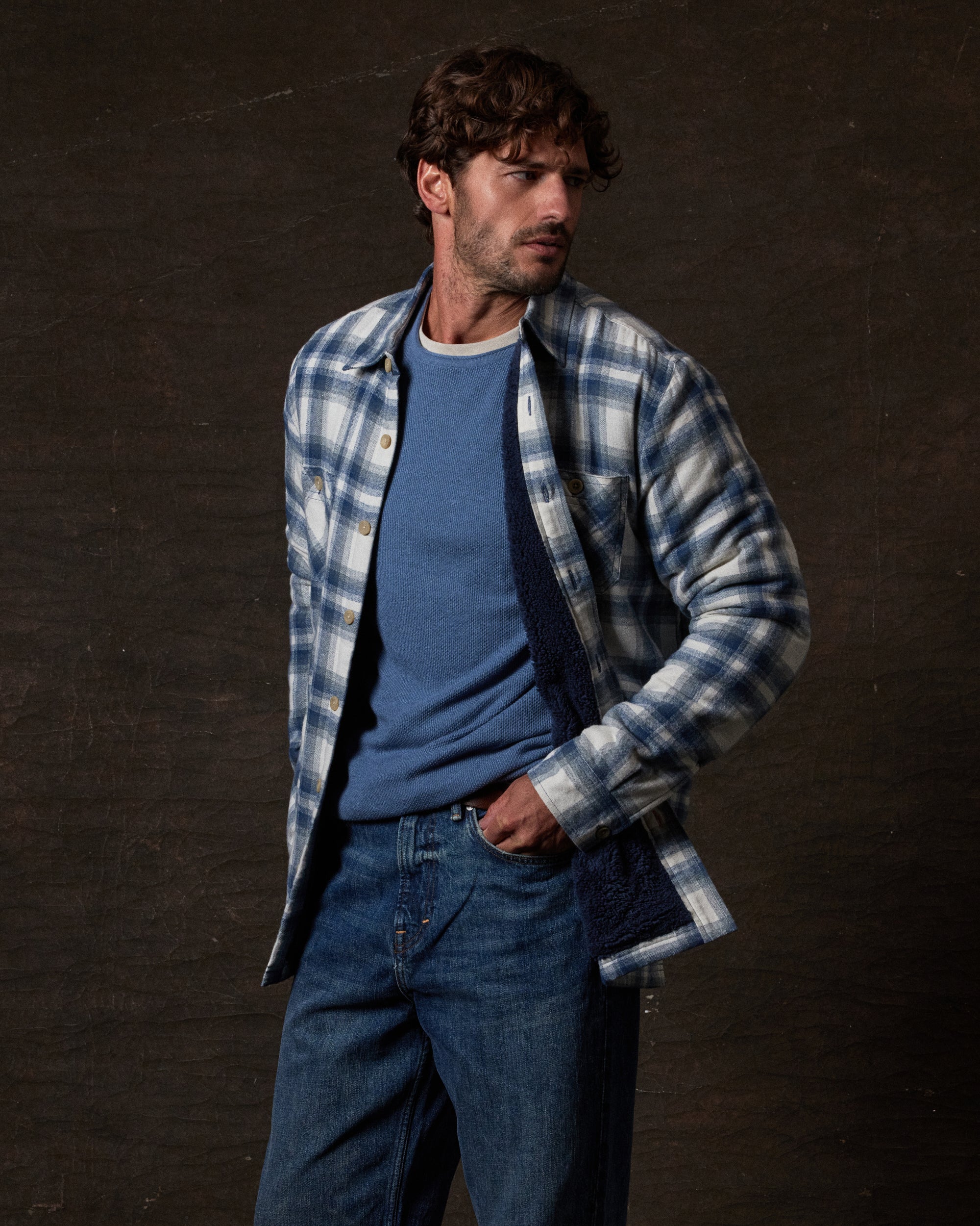Model wearing the Sherpa Lined Flannel Shirt Jacket in Iron Blue over a blue sweater, showcasing its cozy design.