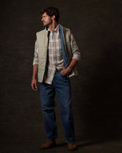 Model showcasing the Matte Coated Shell Puffer Vest in Abbey Stone over a plaid shirt and jeans.