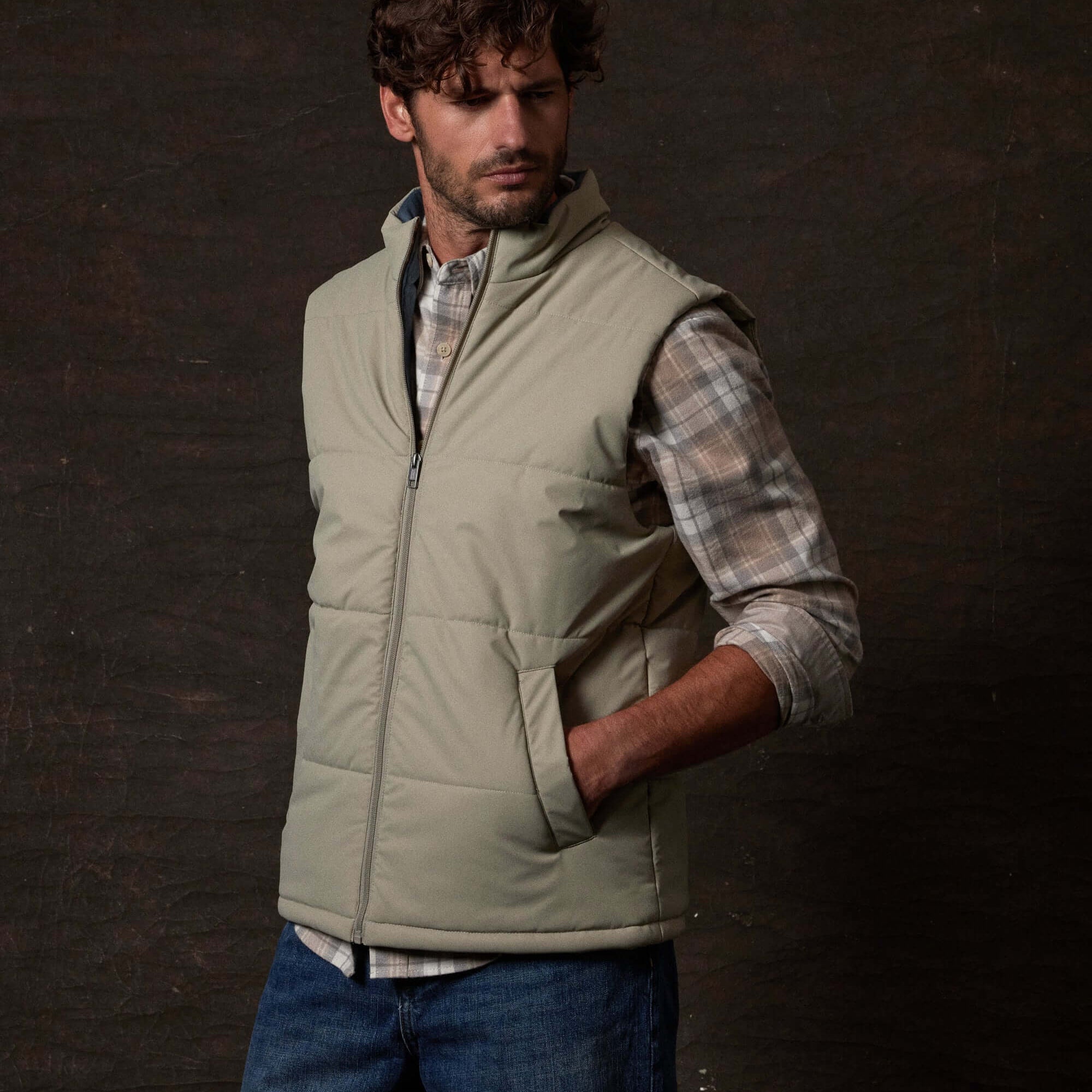 Model wearing a Matte Coated Shell Puffer Vest in Abbey Stone against a dark background, showcasing its sleek design.