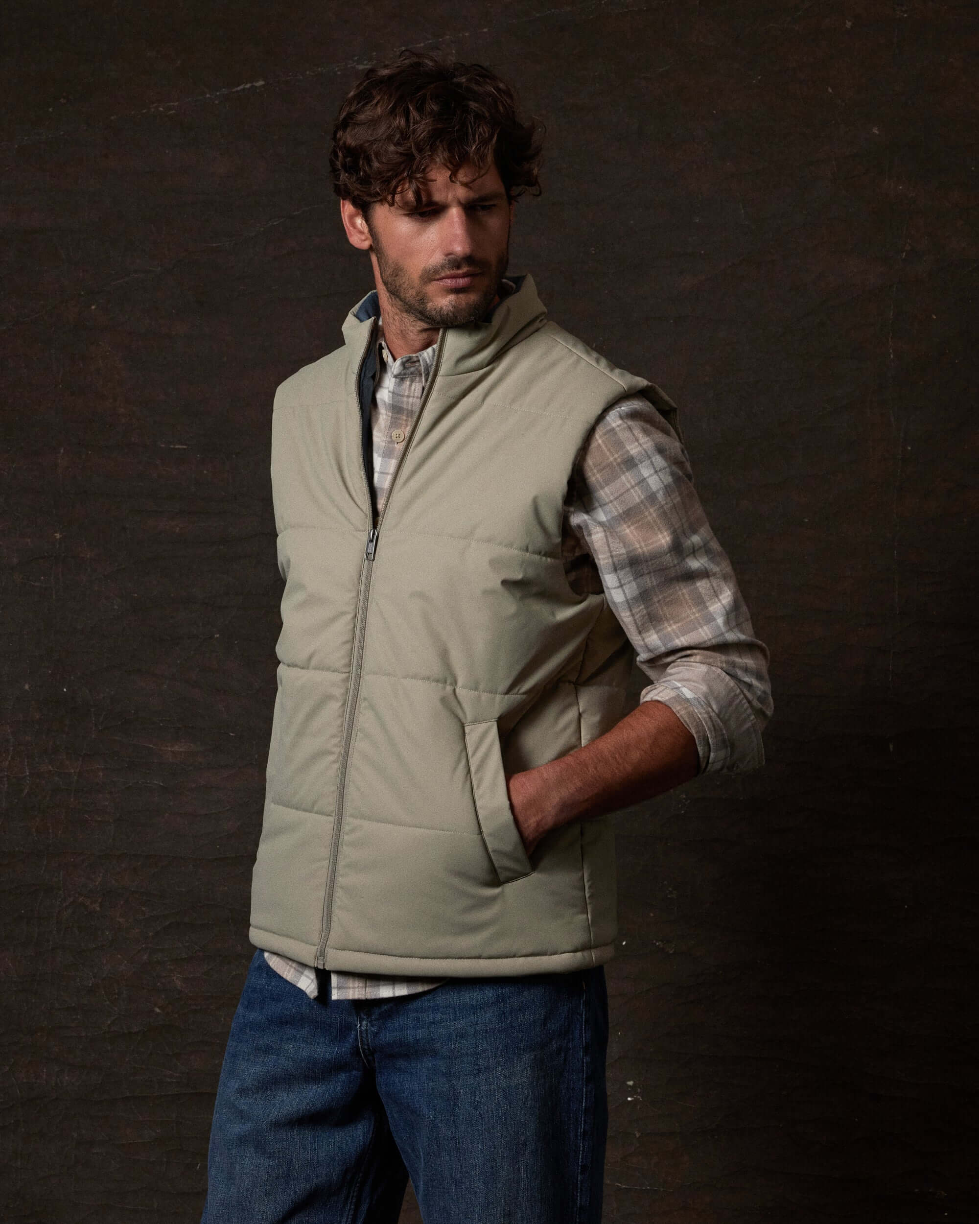 Model wearing a Matte Coated Shell Puffer Vest in Abbey Stone against a dark background, showcasing its sleek design.