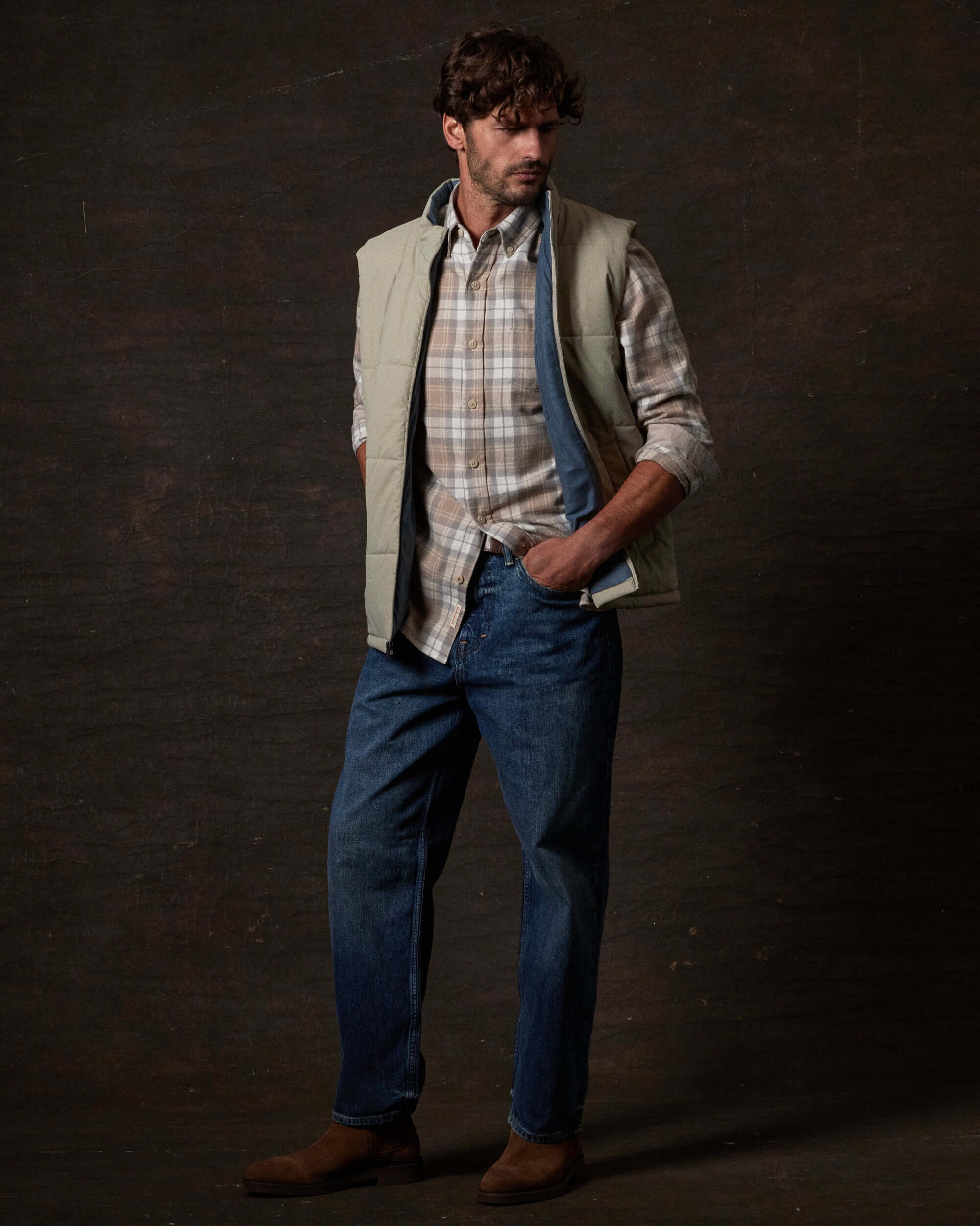 Model wearing Matte Coated Shell Puffer Vest in Abbey Stone with plaid shirt and jeans, showcasing modern rugged utility.