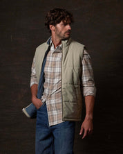 Man modeling a Matte Coated Shell Puffer Vest in Abbey Stone over a plaid shirt, showcasing its modern design and fit.