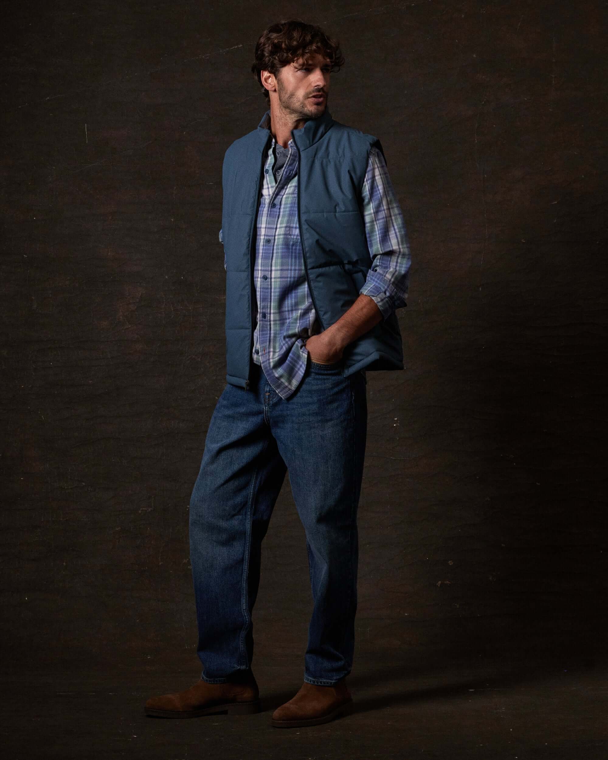 Model wearing Matte Coated Shell Puffer Vest in Slate Blue paired with plaid shirt and jeans.