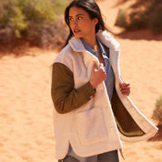 Woman wearing a cozy mixed media quilted jacket with faux shearling, posing in a sandy landscape.