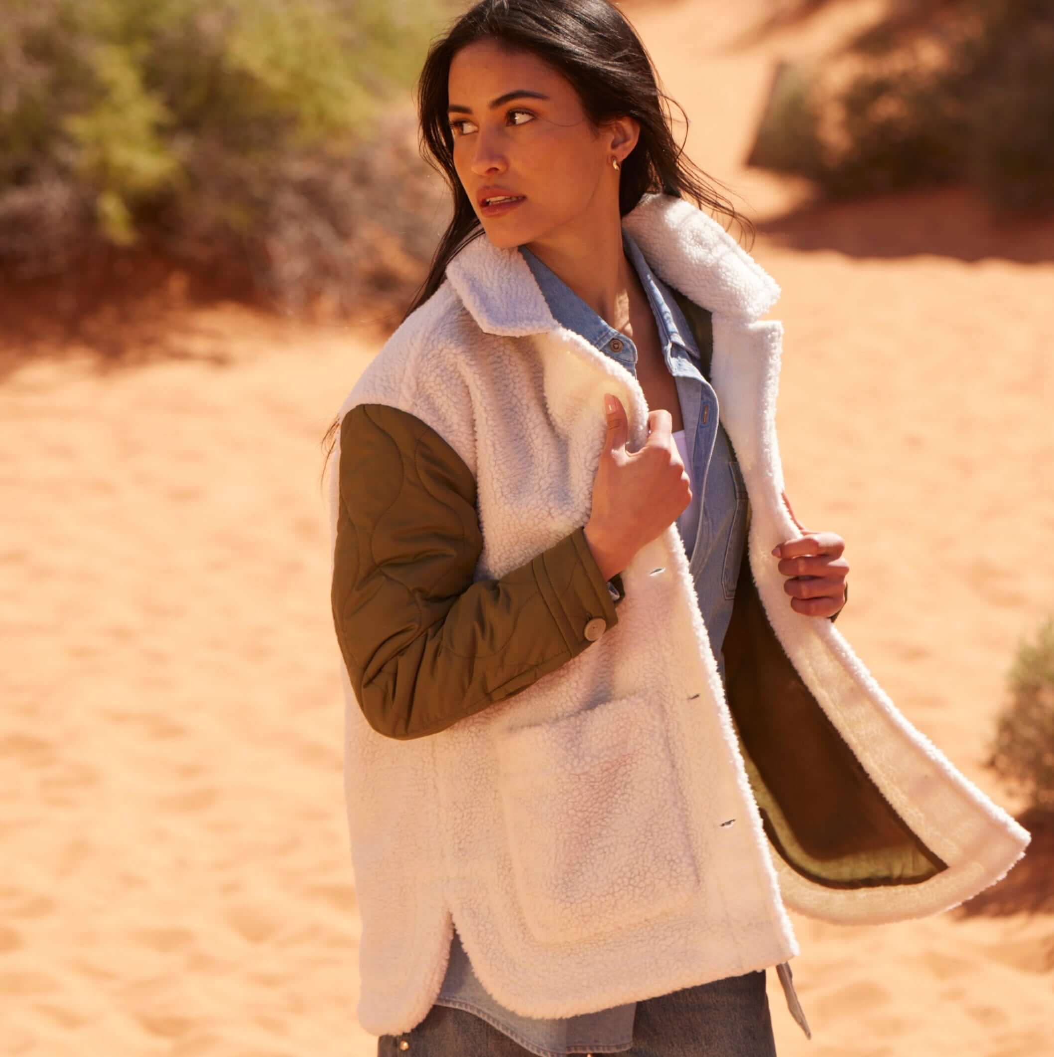 Woman wearing a cozy mixed media quilted jacket with faux shearling, posing in a sandy landscape.