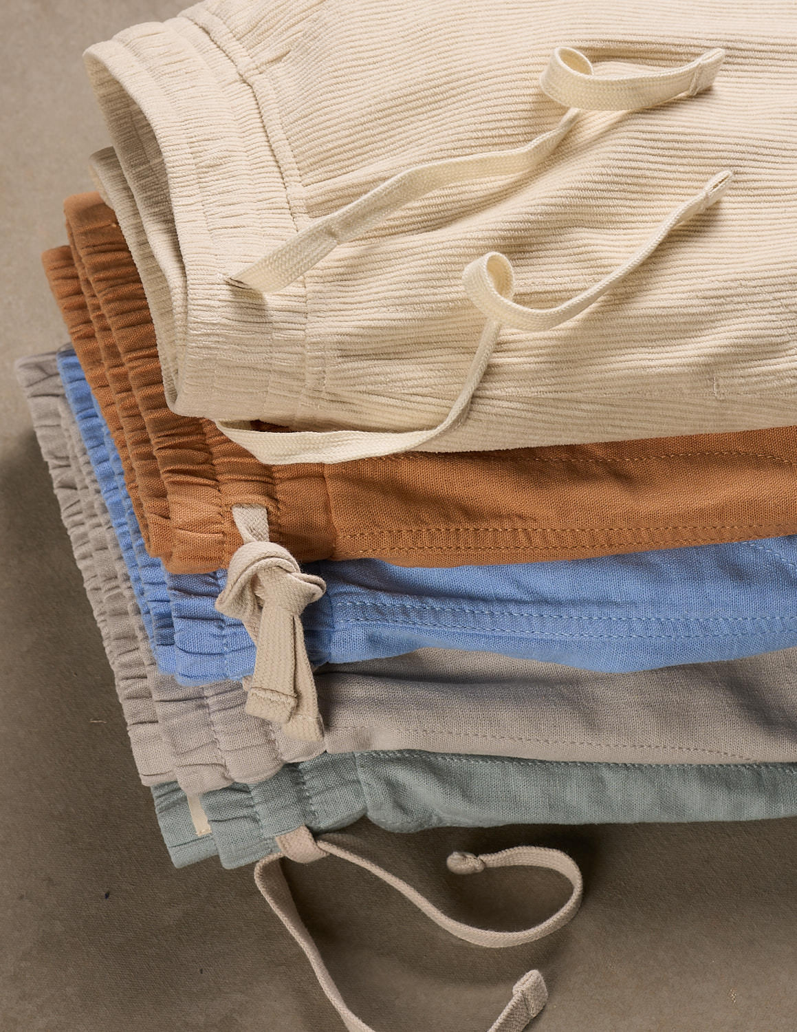Stack of assorted soft ribbed shorts in beige, brown, blue, gray, and mint green hues, featuring drawstring closures.