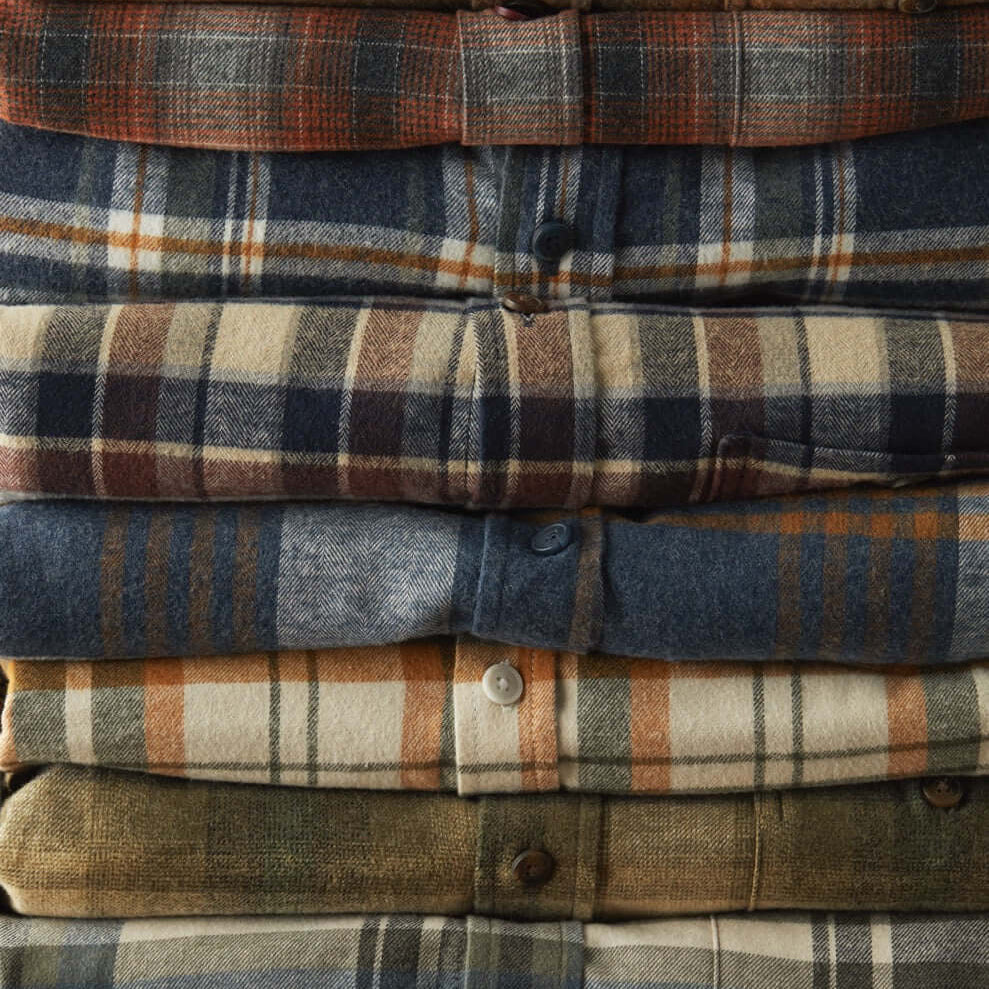 Stack of colorful flannel shirts in various plaid patterns, showcasing texture and cozy design for stylish fall fashion.
