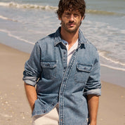 Denim Shirt In Acid Blue worn by a model on the beach, showcasing its soft, faded look and rugged design.