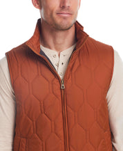 Man wearing a hexagon quilted lightweight vest in caramel cafe, showcasing front zipper and mock-neck design.