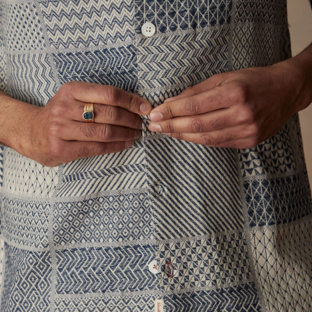 Close-up of a person adjusting buttons on a cream and navy jacquard resort shirt, showcasing textured fabric details.