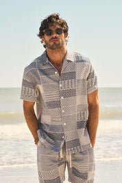 Man wearing a cream and navy jacquard resort shirt, styled for a beach vacation, with sunglasses on.