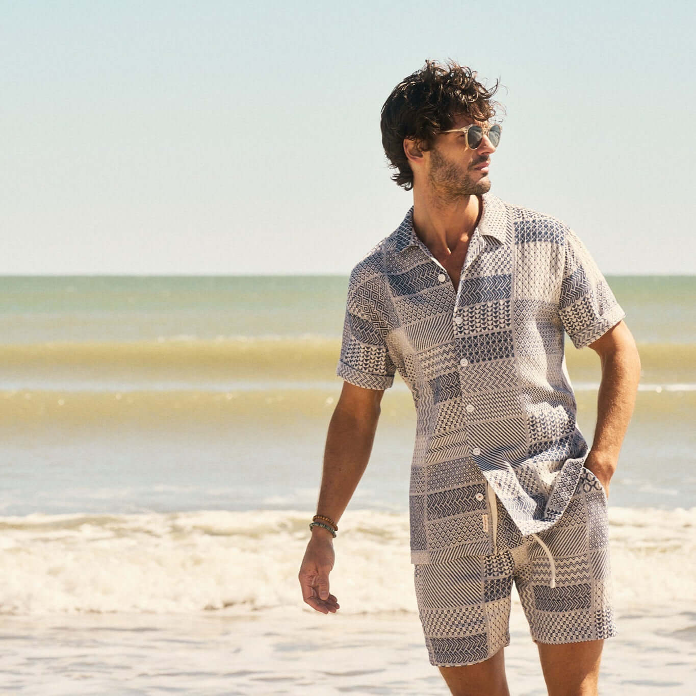 Man wearing a Jacquard Resort Shirt in Cream/Navy on the beach, showcasing a stylish vacation look.