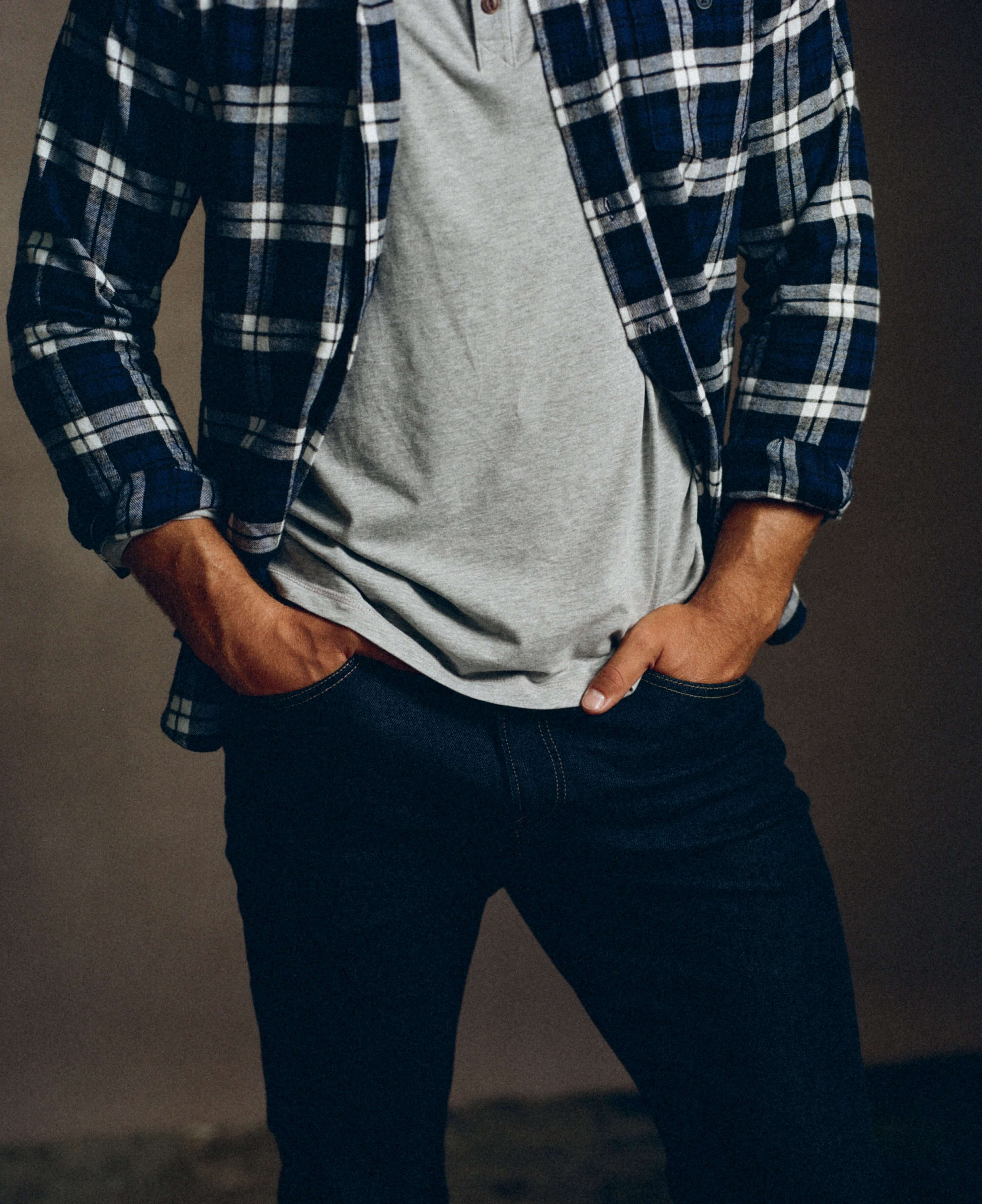 Man wearing a blue plaid long sleeve brushed flannel shirt over a grey t-shirt, styled with dark jeans.