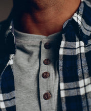 Close-up of a man wearing a blue plaid flannel shirt over a gray henley, showcasing rustic style and soft fabric.