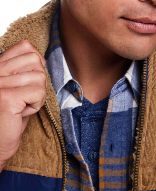 Close-up of a man wearing a blue plaid long sleeve brushed flannel shirt under a tan jacket.