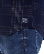Close-up of a blue plaid cord shirt featuring a vintage label, paired with denim for a stylish casual look.