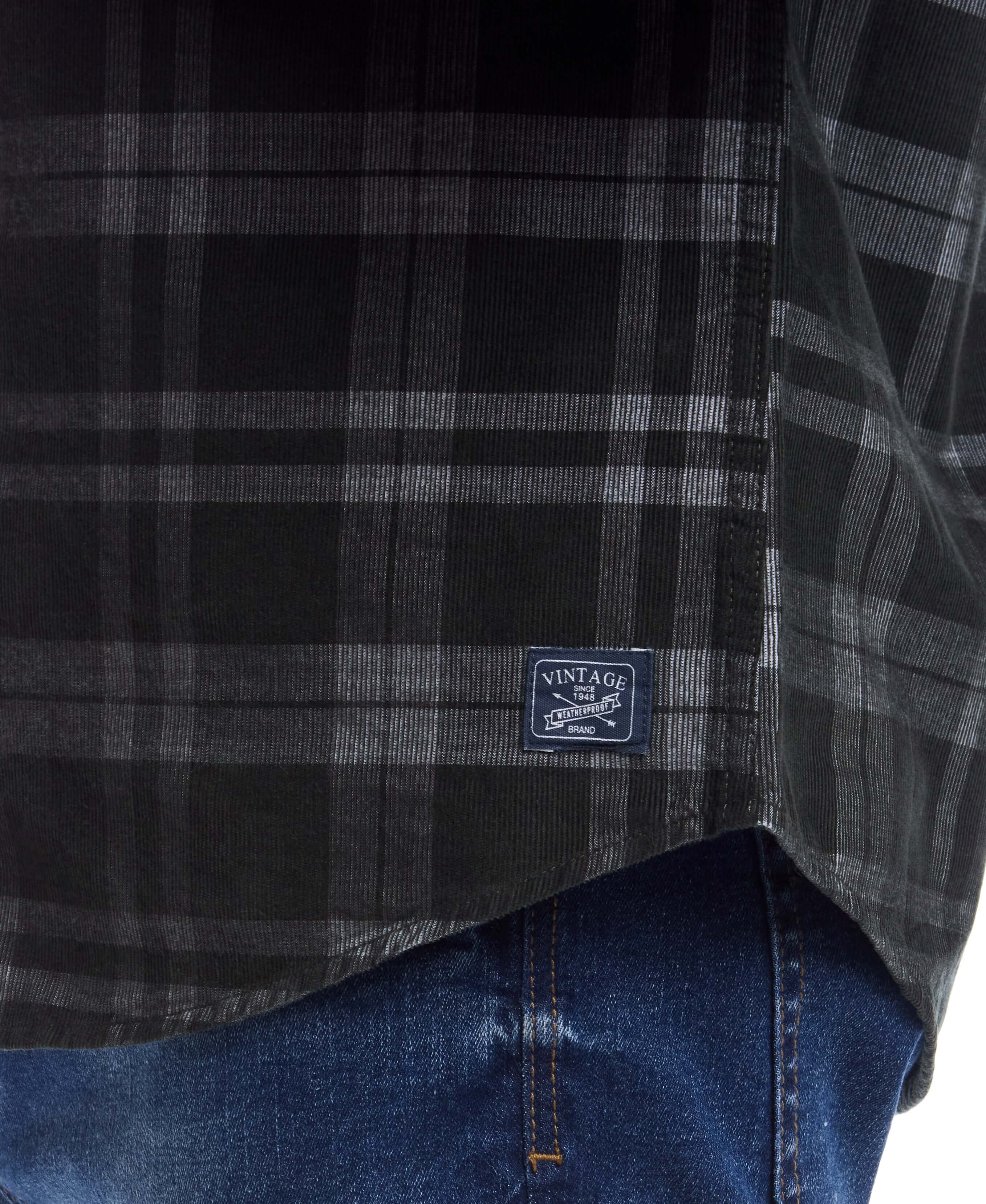 Close-up of a vintage label on a long sleeve plaid cord shirt in forest night, paired with denim jeans.