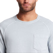 Close-up of a man wearing a dusty blue long sleeve raglan sweatshirt with a crew neck and chest pocket.