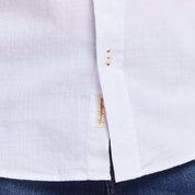 Close-up of a white long sleeve cotton twill shirt showcasing the button front and side label detail.