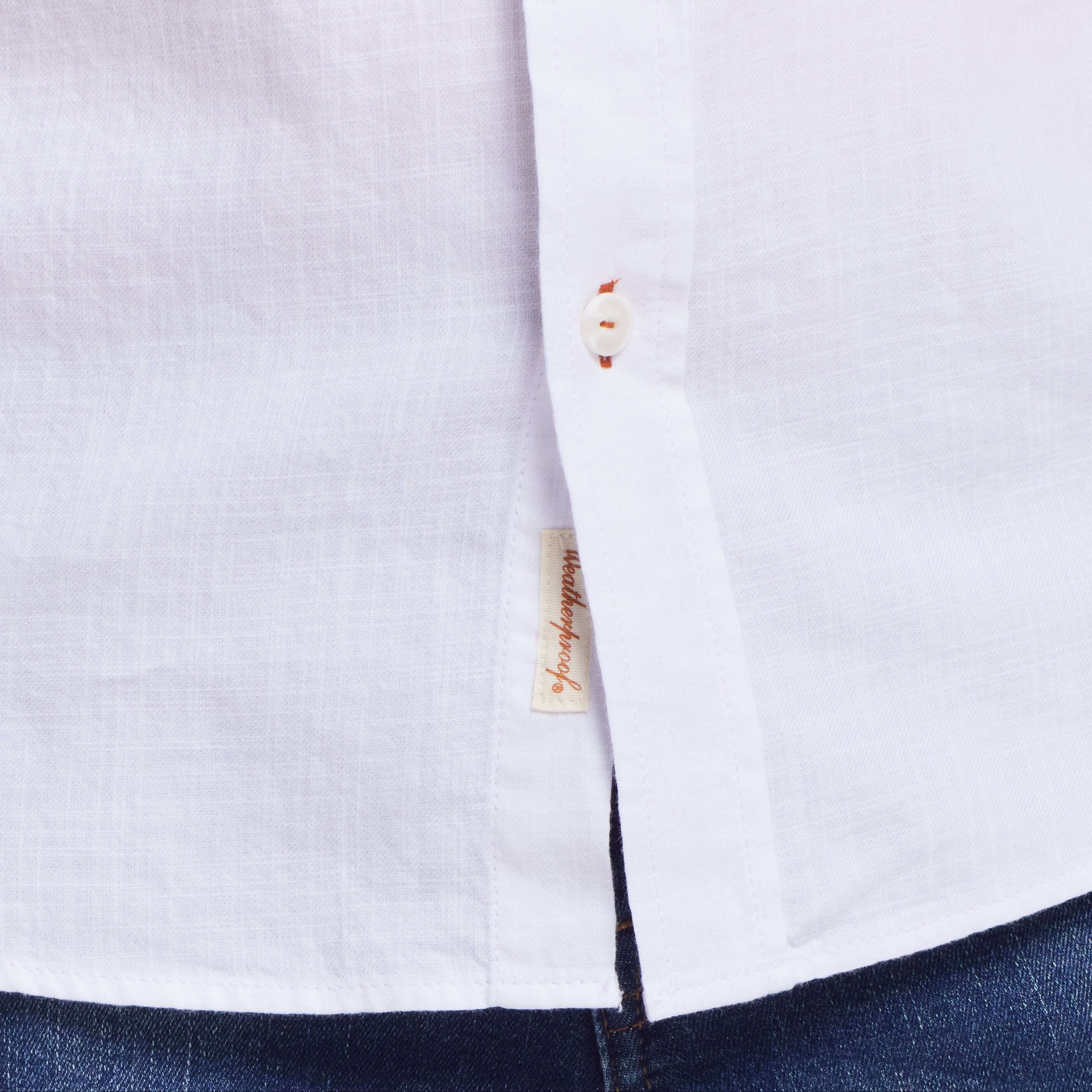 Close-up of a white long sleeve cotton twill shirt showcasing the button front and side label detail.