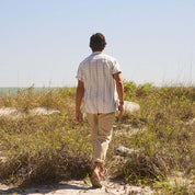 Man in Short Sleeve Aztec Dobby Shirt walking along a sandy path by the beach, showcasing a classic and comfortable style.
