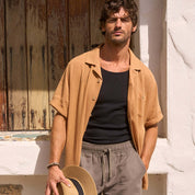 Man wearing a Short Sleeve Cotton Linen Airtex Shirt in Biscuit, styled with shorts and a straw hat.
