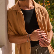 Man in a biscuit short sleeve cotton linen Airtex shirt, featuring a camp collar and button down pocket.