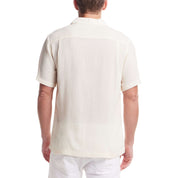 Back view of a man wearing a short sleeve cream Airtex shirt, showcasing its classic vacation style and camp collar.