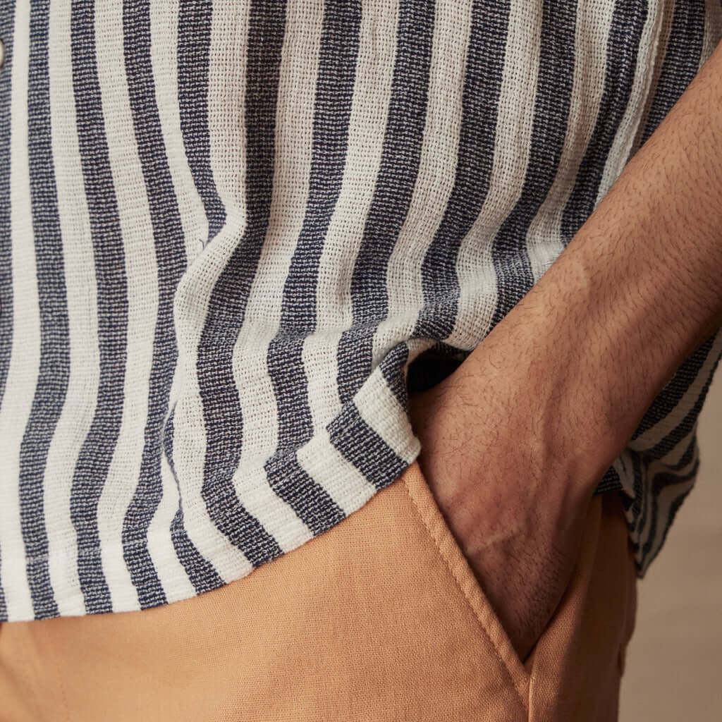 Close-up of a short sleeve cotton linen stripe shirt in Insignia Blue held with one hand in a casual pose.
