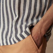 Close-up of a short sleeve cotton linen stripe shirt in Insignia Blue held with one hand in a casual pose.