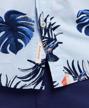 Short sleeve cotton poplin shirt featuring tropical leaves pattern in blue and white, showcasing button-down details.