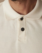 Close-up of an ivory short sleeve honeycomb pique polo shirt featuring a flat ribbed collar and snap placket.