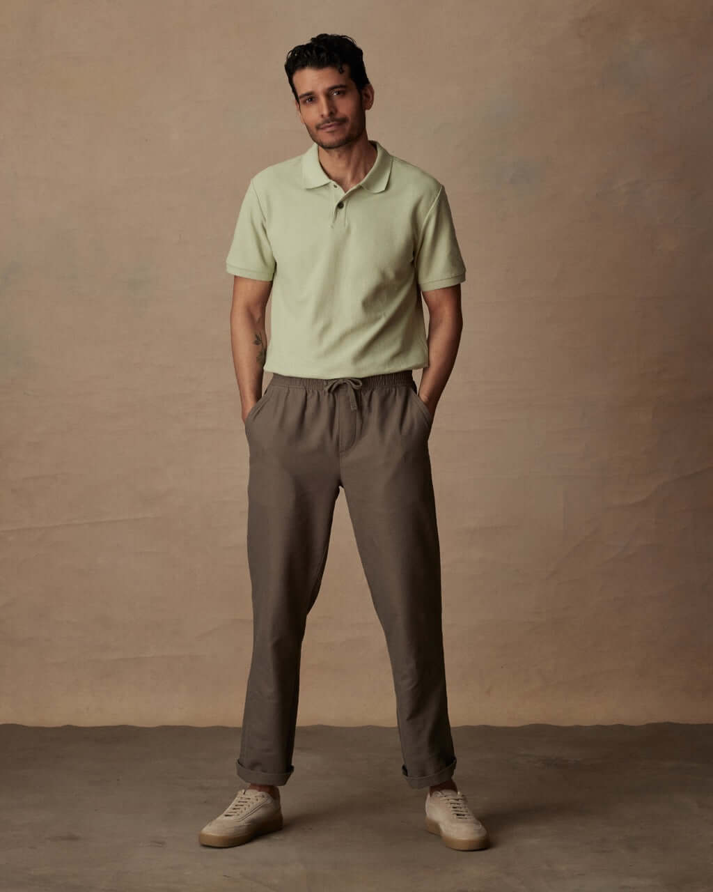 Man wearing light green short sleeve honeycomb pique polo shirt with brown pants against a neutral background.