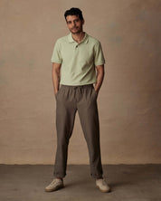 Man wearing light green short sleeve honeycomb pique polo shirt with brown pants against a neutral background.