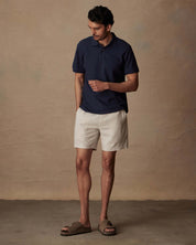 Model wearing a Short Sleeve Honeycomb Pique Polo Shirt in Peacoat, paired with light shorts and sandals.