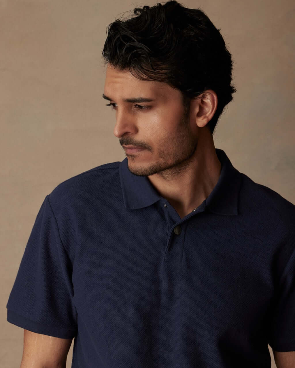 Man in a short sleeve honeycomb pique polo shirt, peacoat color, showcasing classic style and ribbed collar.