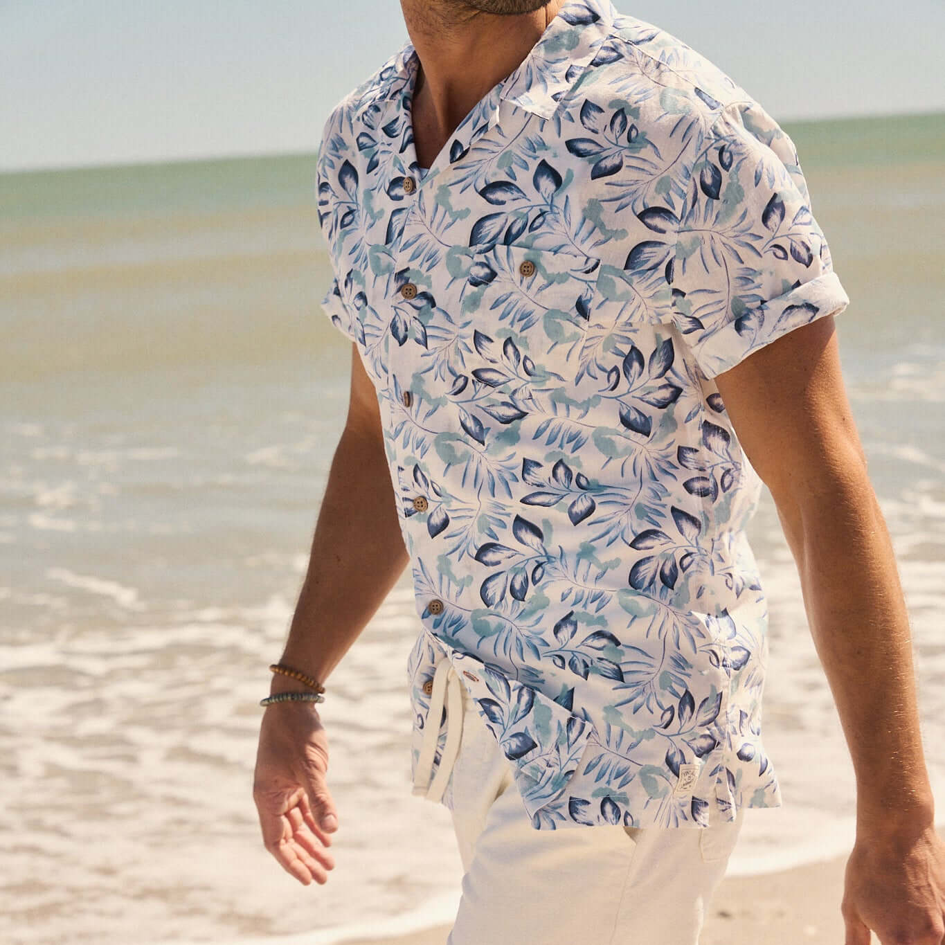 Man walking on the beach in a short sleeve linen cotton camp shirt with a floral print.
