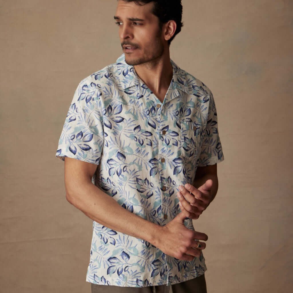 Model wearing short sleeve linen cotton camp shirt in fjord blue with bold print and camp collar.