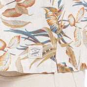 Close-up of short sleeve linen cotton camp shirt in floral print featuring vintage label and vibrant leaf design.