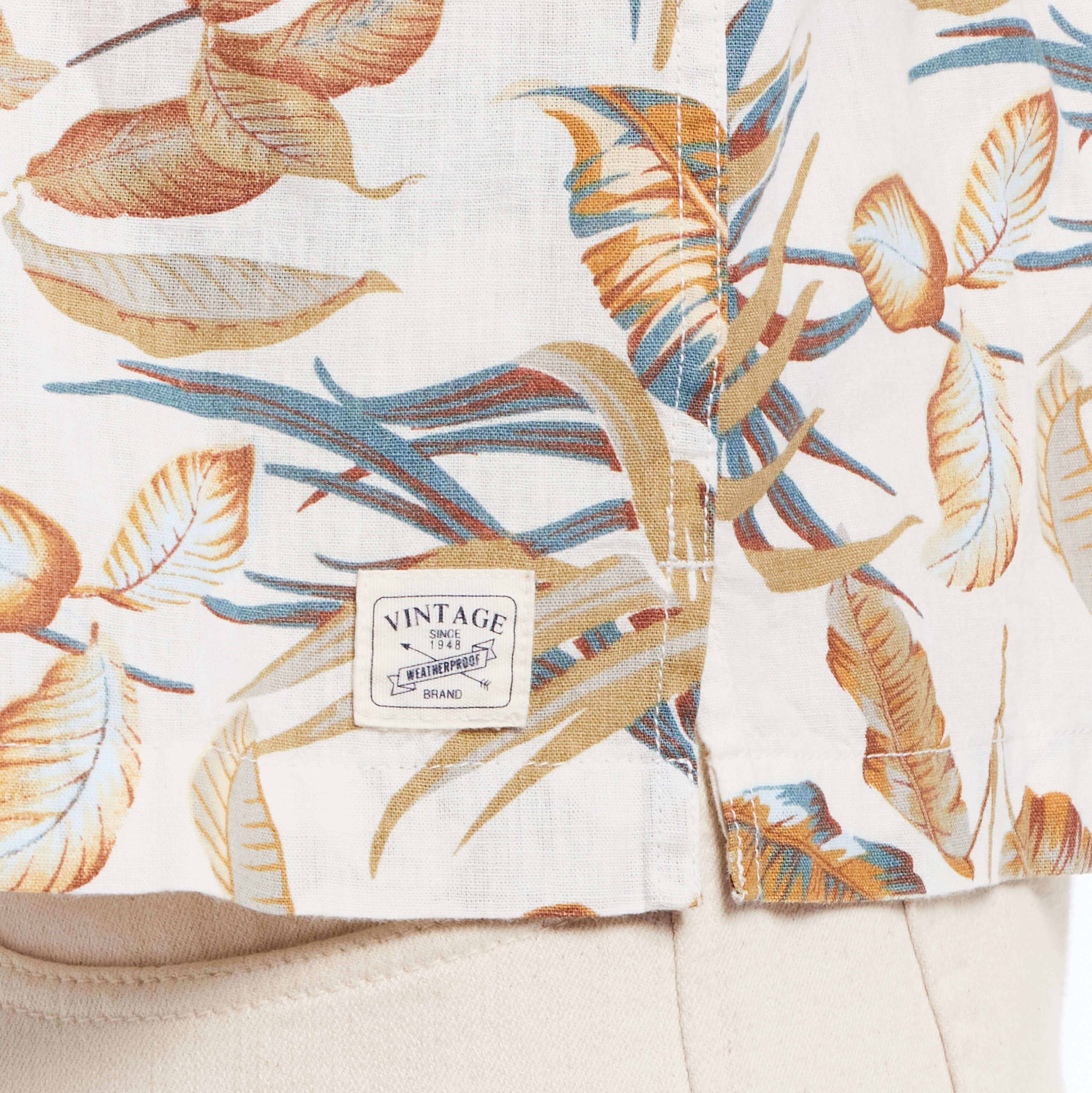 Close-up of short sleeve linen cotton camp shirt in floral print featuring vintage label and vibrant leaf design.