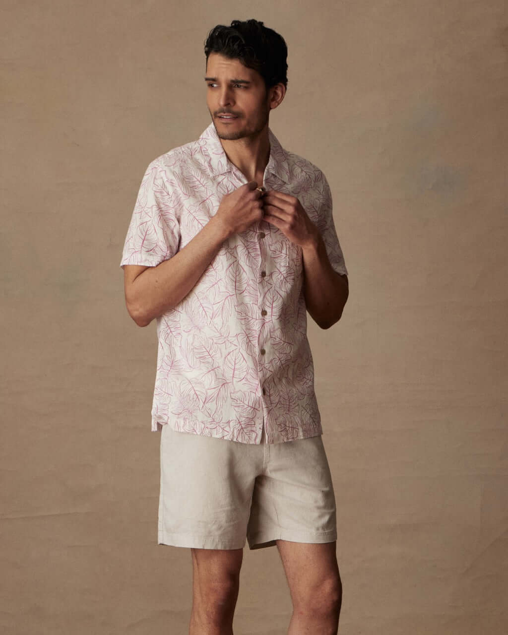 Model wearing a short sleeve linen cotton camp shirt in wild rose with a camp collar and button closure.