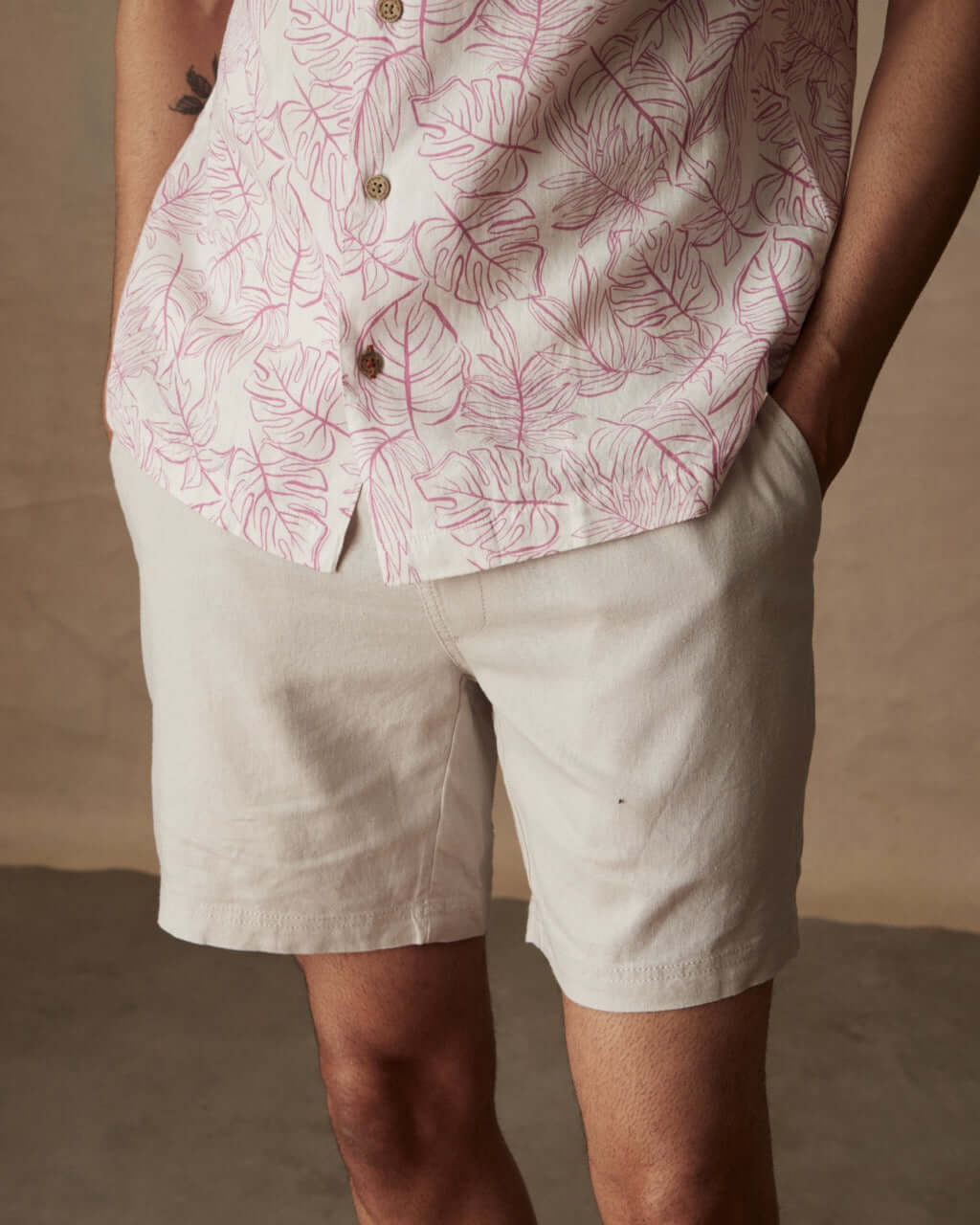 Model wearing a short sleeve linen cotton camp shirt in wild rose with leaf print, paired with white shorts.