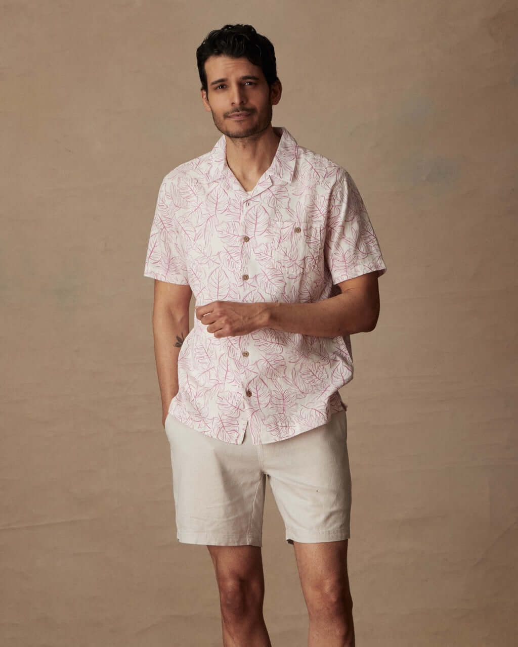 Model wearing a short sleeve linen cotton camp shirt in wild rose with a floral print and shorts.