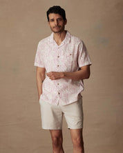 Model wearing a short sleeve linen cotton camp shirt in wild rose with a floral print and shorts.